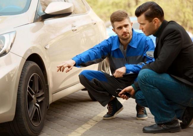 Мужчина показывает на колесо машины Двое мужчин осматривают колеса машины