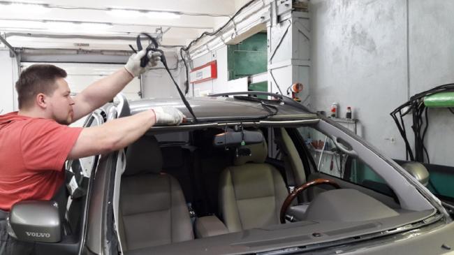 Подготовка поверхности под новое стекло Мужчина чистит периметр лобового стекла