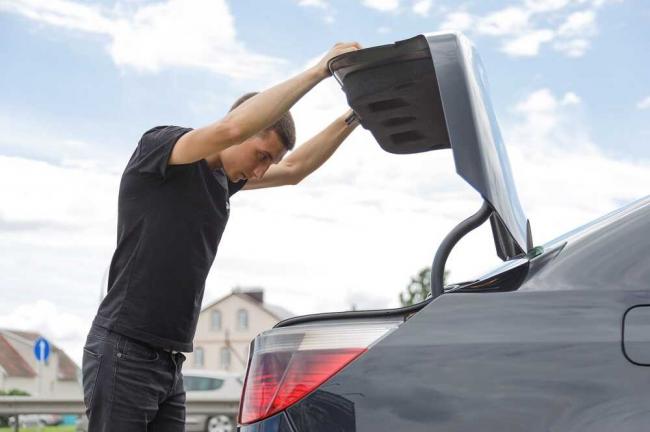 Молодой человек опускает крышку багажника у седана Мужчина закрывает багажник автомобиля